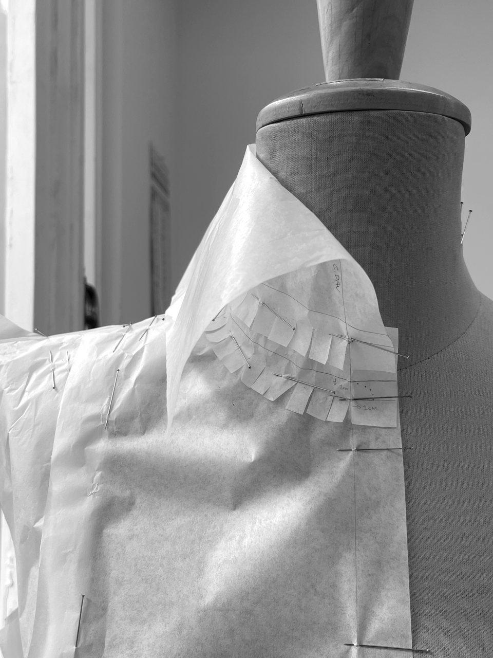 A close view of pattern paper draped on the form at the neckline and shoulder, clip-notched around the curved seam and pinned in a radiating fan