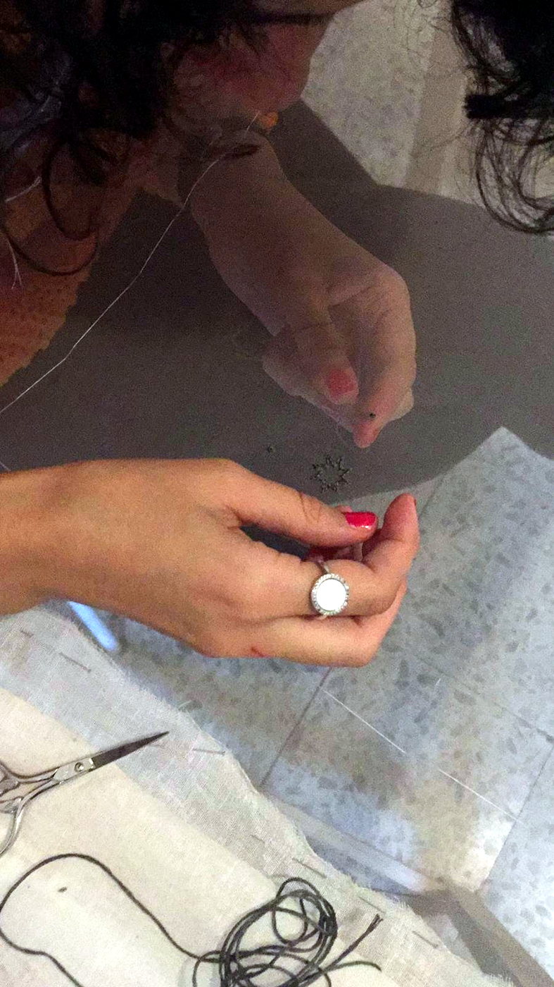 An embroiderer hand-stitching a beaded motif at the bench