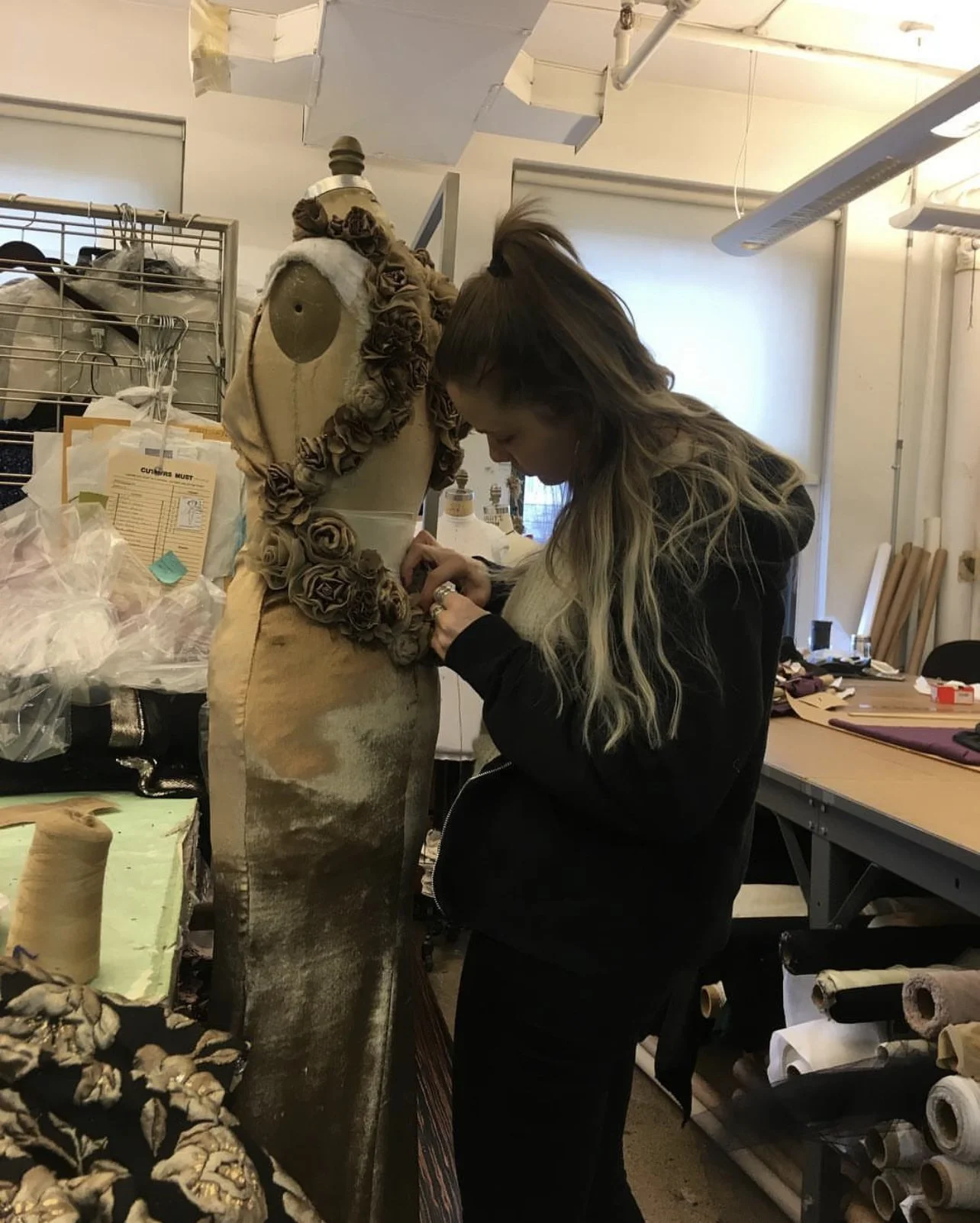 Hands working rolled-fabric roses onto a gown on the stand