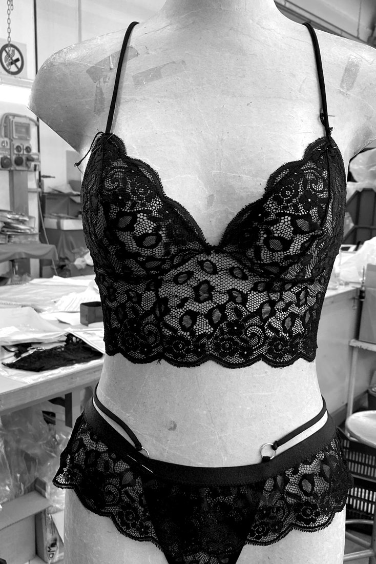 The first sewn sample of the lace bralette on a dress form in the atelier: a scalloped lace long-line bralette with a ruffled lace tanga, gold ring at the waist strap