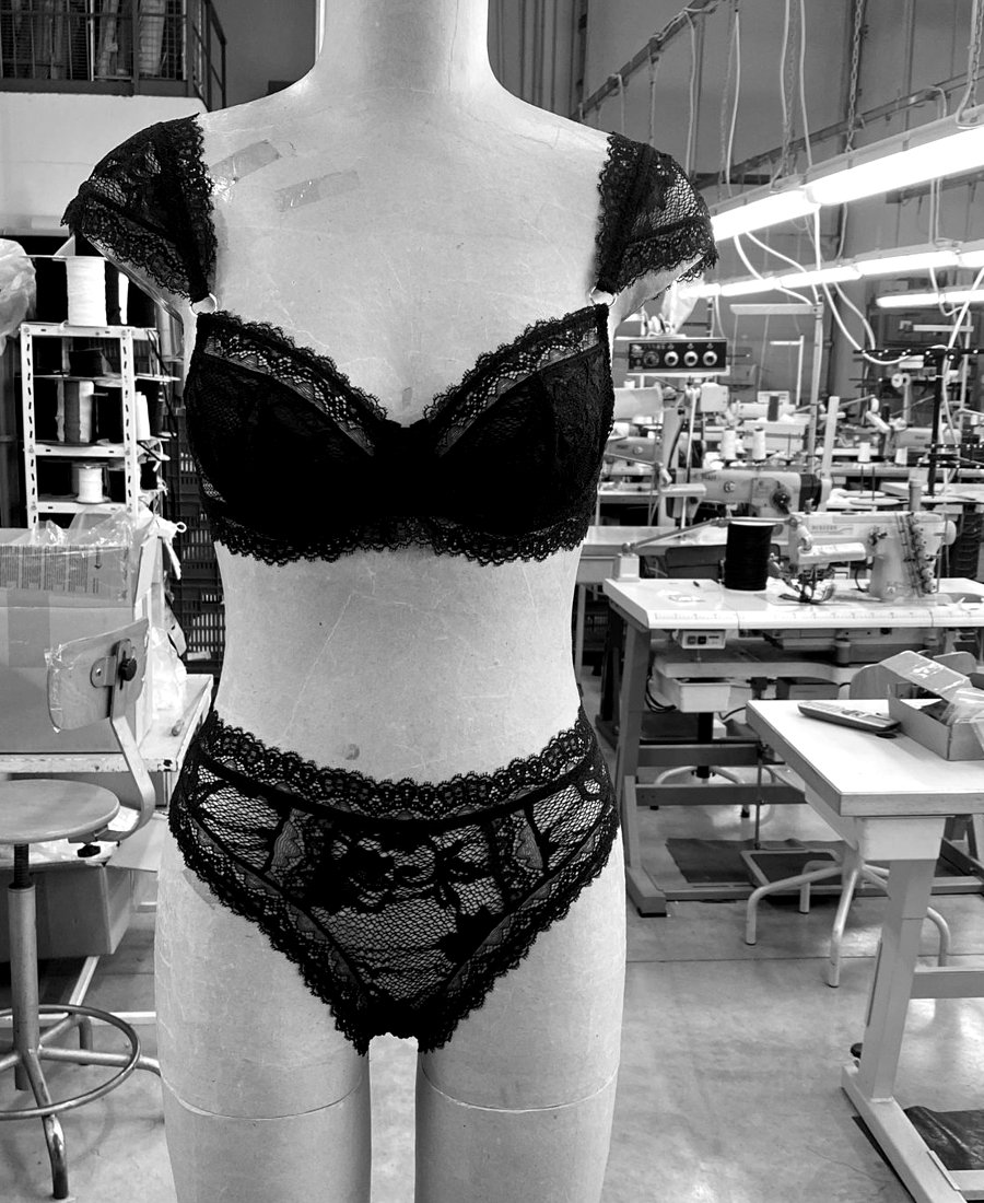 The first sewn sample of the underwire bra on a dress form in the atelier: a black lace underwire bra with cap sleeves worn with a matching lace tanga