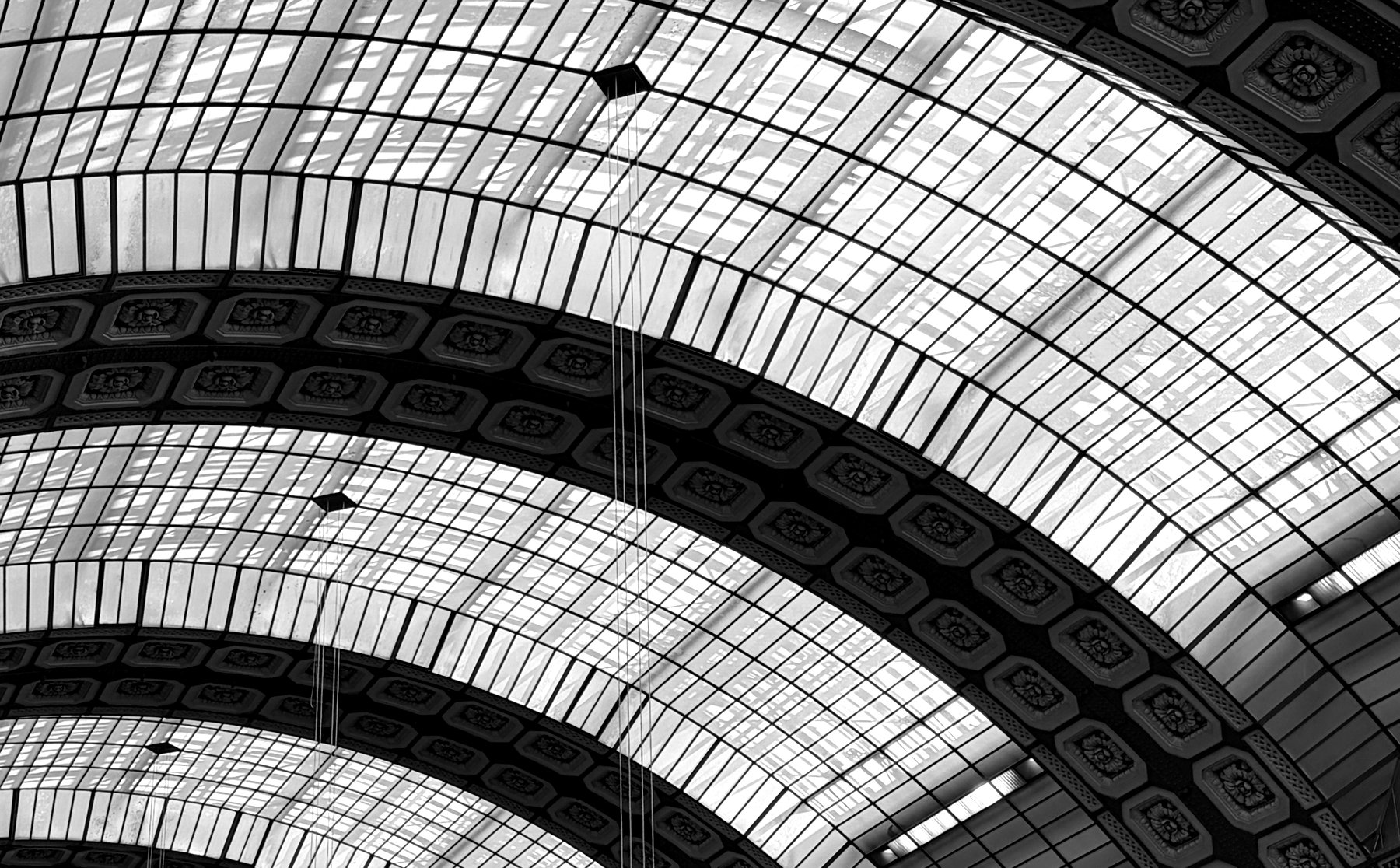 The vaulted, coffered glass-and-iron ceiling of a grand Beaux-Arts hall, its arches and glazing bars sweeping across the frame